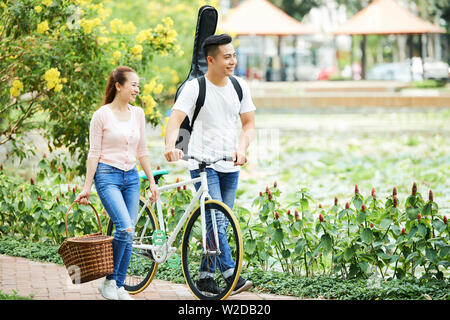 Asian Woman walking in the park jeune homme à la location et de la guitare dans le dos et la femme exerçant son panier pour pique-nique Banque D'Images