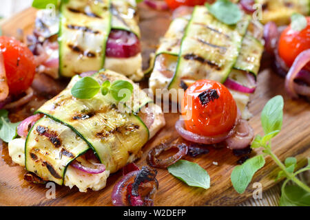 Repas Barbecue végétarien : feta grecque grillé avec oignons rouges enveloppés dans de fines tranches de courgette, servi avec des petites tomates cerises Banque D'Images