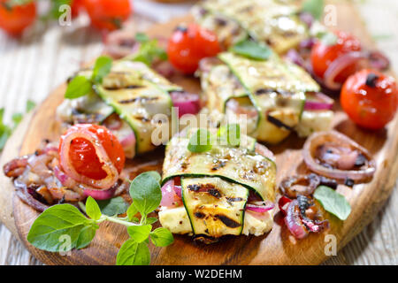 Repas Barbecue végétarien : feta grecque grillé avec oignons rouges enveloppés dans de fines tranches de courgette, servi avec des petites tomates cerises Banque D'Images