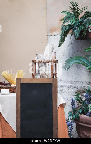 Style Italien vide du vrai tableau noir en face de table avec des pâtes et du pain, entouré de plantes Banque D'Images