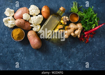 Mettre les ingrédients bruts, cuisine végétarienne La cuisine indienne Aloo Gobi sur fond noir en sombre Banque D'Images