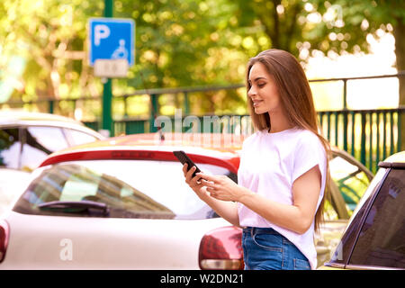 Shot of young woman standing dans la rue à côté de sa voiture et la messagerie texte. Banque D'Images