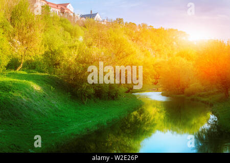 Petite rivière calme à Kamianets Podilskyi avec réflexion parmi l'herbe verte fraîche, arbres et arbustes Banque D'Images