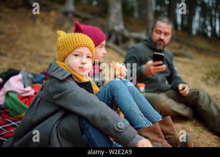 Jolie petite soeurs et leur père having picnic par un feu par une froide journée d'automne. Les enfants s'amuser au feu de camp. Camping avec les enfants dans la forêt d'automne Banque D'Images