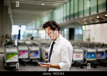 Businessman checking son téléphone cellulaire dans un aéroport. Banque D'Images