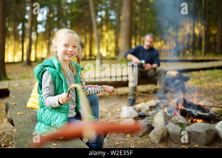 Jolie petite soeurs et leur père les guimauves grillées sur des bâtons à feu. Les enfants s'amuser au feu de camp. Camping avec les enfants dans la forêt de l'automne. F Banque D'Images