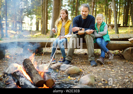 Jolie petite soeurs et leur père les guimauves grillées sur des bâtons à feu. Les enfants s'amuser au feu de camp. Camping avec les enfants dans la forêt de l'automne. F Banque D'Images