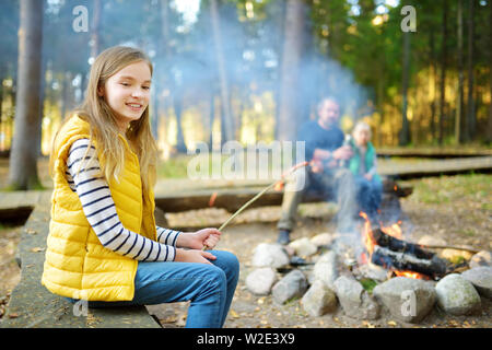 Jolie petite soeurs et leur père les guimauves grillées sur des bâtons à feu. Les enfants s'amuser au feu de camp. Camping avec les enfants dans la forêt de l'automne. F Banque D'Images