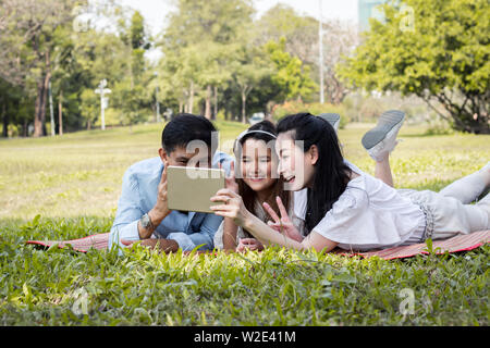 Parents et enfants jouent le comprimé sur le tapis dans le parc. Père et mère sont l'enseignement à l'aide de la tablette. Les filles apprennent à partir d'un tabl Banque D'Images