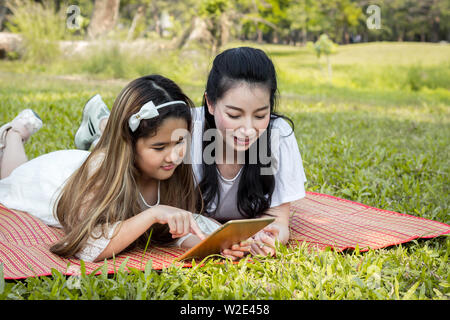 Mère et enfants jouent le comprimé sur le tapis dans le parc. La mère sont l'enseignement par l'utilisation de la tablette. Les filles apprennent à partir d'un comprimé qui moth Banque D'Images