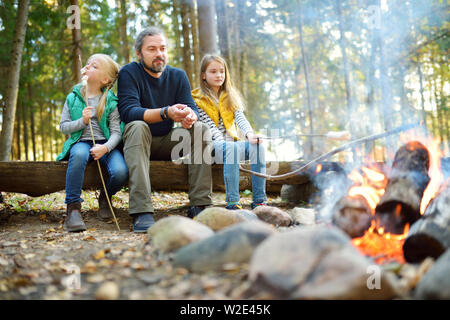 Jolie petite soeurs et leur père les guimauves grillées sur des bâtons à feu. Les enfants s'amuser au feu de camp. Camping avec les enfants dans la forêt de l'automne. F Banque D'Images