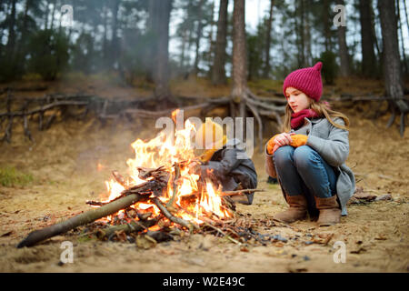 Deux jolies jeunes femmes assis par un feu par une froide journée d'automne. Les enfants s'amuser au feu de camp. Camping avec les enfants dans la forêt de l'automne. Loisirs en famille avec Banque D'Images