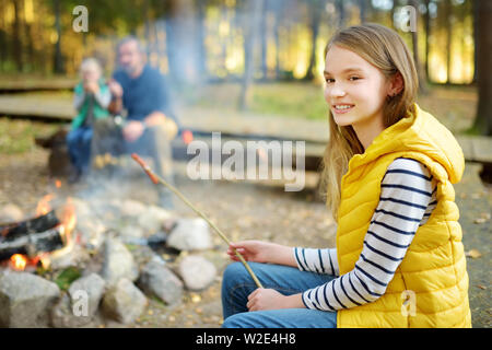 Jolie petite soeurs et leur père les guimauves grillées sur des bâtons à feu. Les enfants s'amuser au feu de camp. Camping avec les enfants dans la forêt de l'automne. F Banque D'Images