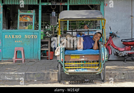 Yogyakarta, Indonésie - yogyakarta di/10 novembre 2015 : un becak driver dormir dans son véhicule sur Jalan lempuyangan en face d'un restaurant Banque D'Images