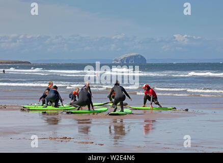 Belhaven Bay, Dunbar, de l'Écosse. 8 juillet 2019. Les enfants peuvent profiter d'apprentissage de surf et bodyboard. Alors qu'une mère en a plein les bras et un jeune garçon profite de conditions de vent pour voler son cerf-volant en face de la Bass Rock, plus les tout-petits jouer dans le sable humide. Banque D'Images