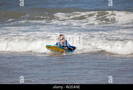 Belhaven Bay, Dunbar, de l'Écosse. 8 juillet 2019. Les enfants peuvent profiter d'apprentissage de surf et bodyboard. Alors qu'une mère en a plein les bras et un jeune garçon profite de conditions de vent pour voler son cerf-volant en face de la Bass Rock, plus les tout-petits jouer dans le sable humide. Banque D'Images