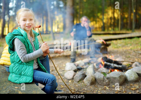 Jolie petite soeurs et leur père les guimauves grillées sur des bâtons à feu. Les enfants s'amuser au feu de camp. Camping avec les enfants dans la forêt de l'automne. F Banque D'Images