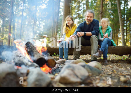 Jolie petite soeurs et leur père les guimauves grillées sur des bâtons à feu. Les enfants s'amuser au feu de camp. Camping avec les enfants dans la forêt de l'automne. F Banque D'Images