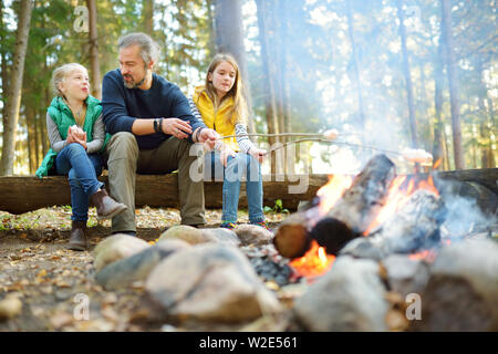 Jolie petite soeurs et leur père les guimauves grillées sur des bâtons à feu. Les enfants s'amuser au feu de camp. Camping avec les enfants dans la forêt de l'automne. F Banque D'Images