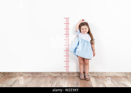 Petite fille blonde la mesure de hauteur sur mur blanc Banque D'Images