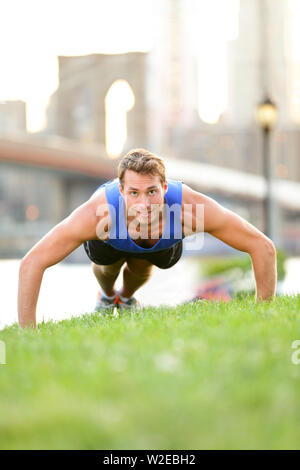 Push-ups - homme de la formation dans la ville de New York, Brooklyn. Remise en forme de sexe masculin faisant pousser l'athlète entraînement Crossfit en plein air avec pont de Brooklyn et Manhattan skyline en arrière-plan. Remise en forme mâle modèle. Banque D'Images