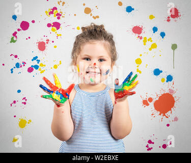 Smiling little girl avec les mains dans la peinture sur mur peint Banque D'Images