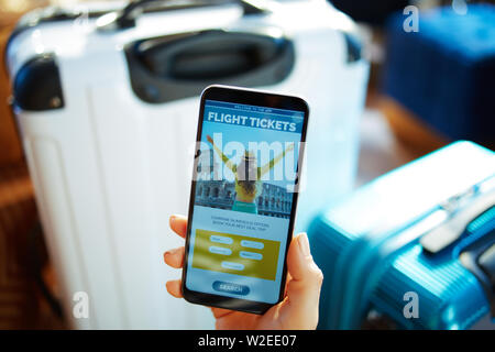 Image main de femme libre de smartphone avec près de trolley sacs chez maison moderne dans la région ensoleillée chaude journée d'été réservation billet d'avion en ligne. Banque D'Images