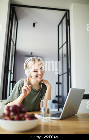 Young smiling woman showing geste de paix tout en regardant son ami sur l'écran de l'ordinateur portable au cours de la communication en ligne Banque D'Images