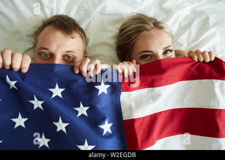 Jeune couple couvrant par drapeau américain tout en étant allongé sur le lit et regarde Banque D'Images