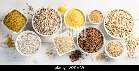 Sélection de grains entiers dans des bols blancs - riz, avoine, sarrasin, boulgur, porridge, orge, quinoa, amarante, Banque D'Images