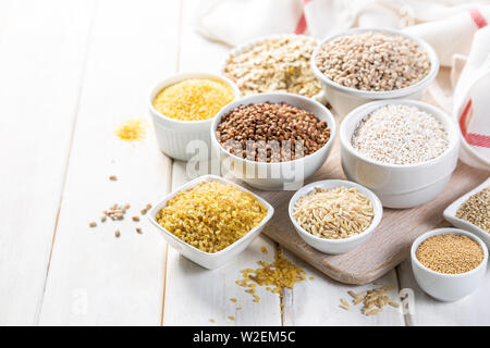Sélection de grains entiers dans des bols blancs - riz, avoine, sarrasin, boulgur, porridge, orge, quinoa, amarante, Banque D'Images