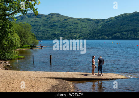 Jeune couple debout sur les rives du Loch Lomond à Tarbet en Écosse, au Royaume-Uni Banque D'Images