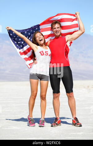 Encourager les athlètes américains USA personnes tenant un drapeau célébrant heureux avec large geste après l'exécution. Jeune couple multiculturel runner fitness en extérieur dans la célébration enthousiaste de la nature désert chaud. Banque D'Images