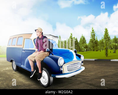 Asian man in hat avec sac à dos, assis sur le capot de la voiture de route avec des arbres verts et fond de ciel bleu. Concept de voyage Banque D'Images