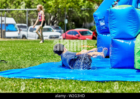 Prescott, Arizona, USA-Juillet 6, 2019 : jeune garçon faisant glisser et tomber en sortant un toboggan gonflable à la guerre de l'eau, sur le Mile haut Moyen-Sc Banque D'Images