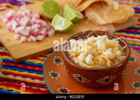 La cuisine mexicaine, poulet pozole servis avec des radis, des citrons et des toasts, le Chili et l'origan árbol de avec un arrière-plan mexicaines colorées. Banque D'Images