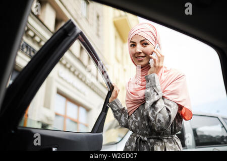 Cheerful pretty young woman in hijab ouverture porte de la voiture et à la recherche au camer Banque D'Images