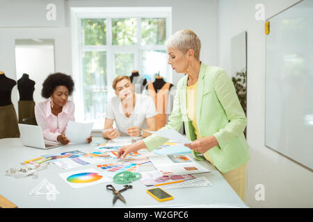 Designer de mode. Concentrés short-haired blonde woman debout à une table de coupe dans un studio des créateurs de mode Banque D'Images