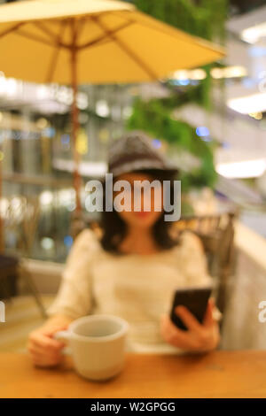Vertical image de femme floue abstraite avec une tasse de café en regardant son téléphone cellulaire dans le café Banque D'Images