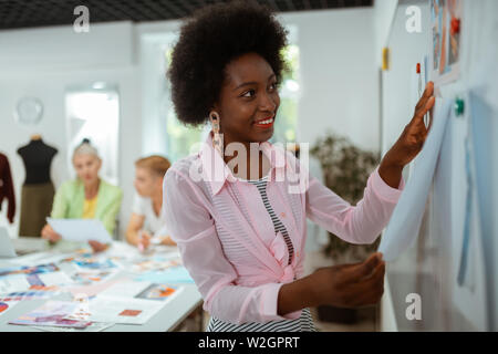 Des croquis sur le tableau blanc. Closeup portrait of a smiling Young Fashion designer pinning ses croquis sur le tableau blanc magnétique dans un studio Banque D'Images