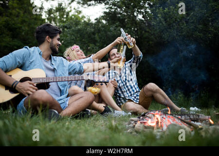 Groupe d'amis camping.Ils sont assis autour d'un feu de camp, jouer de la guitare Banque D'Images