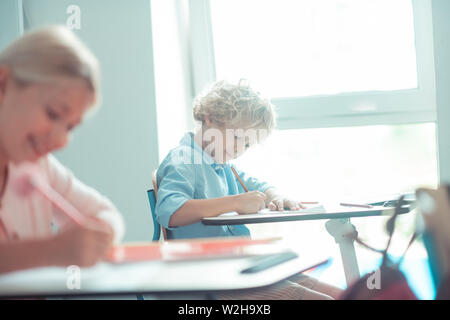 Garçon aux cheveux Blond assis près de la fenêtre de la classe. Banque D'Images