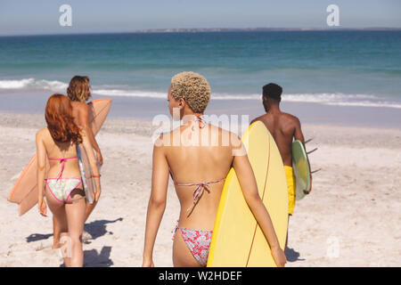 Groupe d'amis à marcher avec une planche de surf sur la plage Banque D'Images