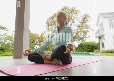 Active senior woman doing yoga sur tapis d'exercice dans le porche, à la maison Banque D'Images