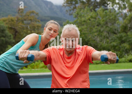 Entraîneur féminin senior actif aidant à exercer avec haltères Banque D'Images