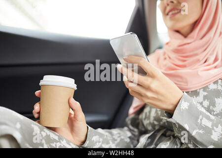 Close-up of smiling femme musulmane dans hijab assis dans la cabine et de boire du café tout en surfant sur le net gadget Banque D'Images