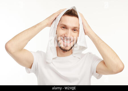 Jeune homme barbu sur le fond blanc rubbs la tête avec une serviette blanche. Banque D'Images