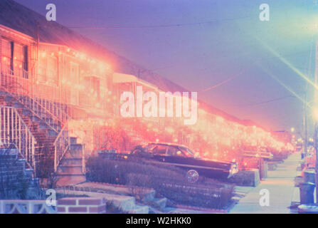 Les lumières de Noël sur les maisons et les voitures garées dans l'entrée de la maison de banlieue en 1965 Banque D'Images