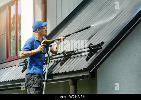 Homme debout sur l'échelle et nettoyer la maison avec toit en métal nettoyeur haute pression Banque D'Images