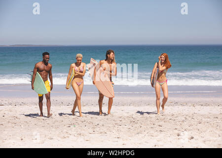 Groupe d'amis à marcher avec une planche de surf sur la plage Banque D'Images